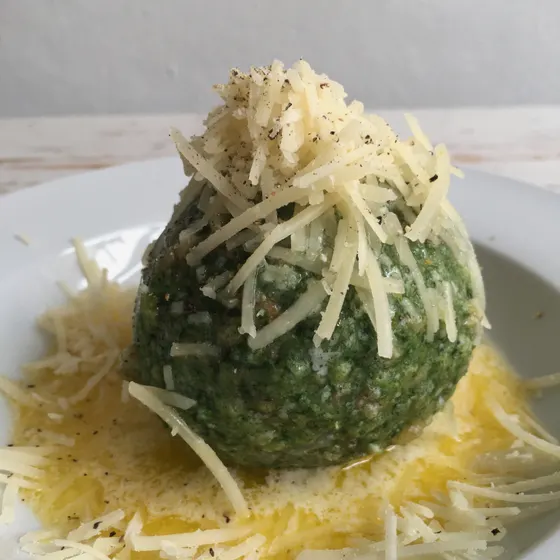 Ein grüner Kräuterknödel mit geriebenem Käse auf einem Teller