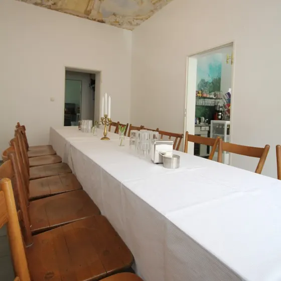 Eine lange, weiß gedeckte Tafel mit Kerzen und Gläsern im Gastraum