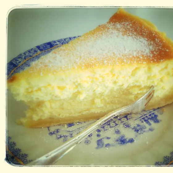 Ein Stück Käsekuchen mit Puderzucker auf einem blau gemusterten Teller