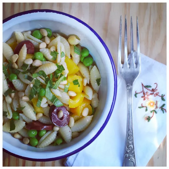 Nudelsalat mit Erbsen, Pinienkernen und Oliven in einer Emailleschüssel, daneben eine Gabel