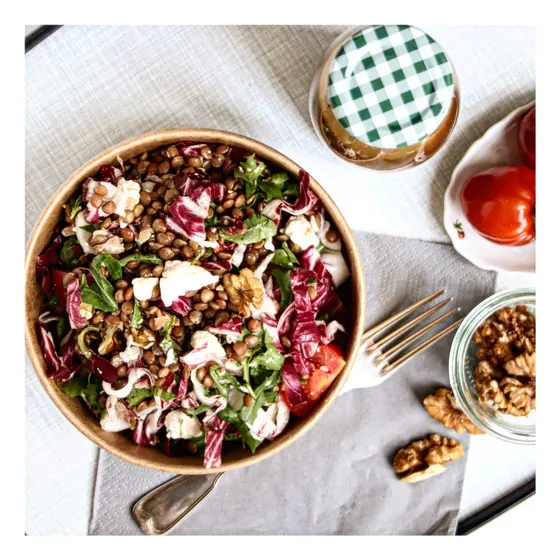 Eine Schüssel Linsensalat mit Radicchio und Walnüssen, daneben Gläser und Besteck