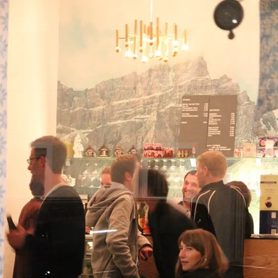 Gäste stehen und sitzen vor der Theke, an der Wand ein Bergpanorama