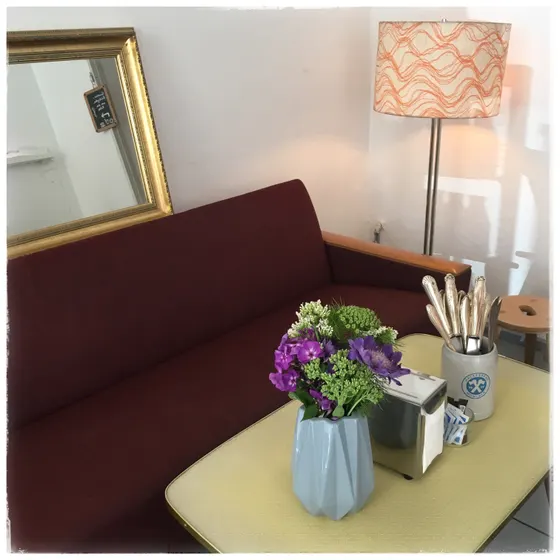 Die Sitzecke im Café: rote Polsterbank, Stehlampe, Spiegel und Blumen auf dem Tisch